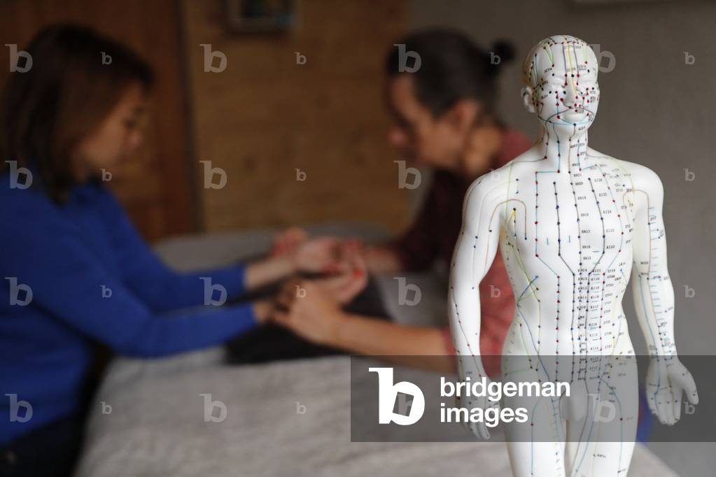 Traditional chinese medecine.  Practitioner checking pulse of young woman to define disease.  A male model with marked acupuncture points.  France.