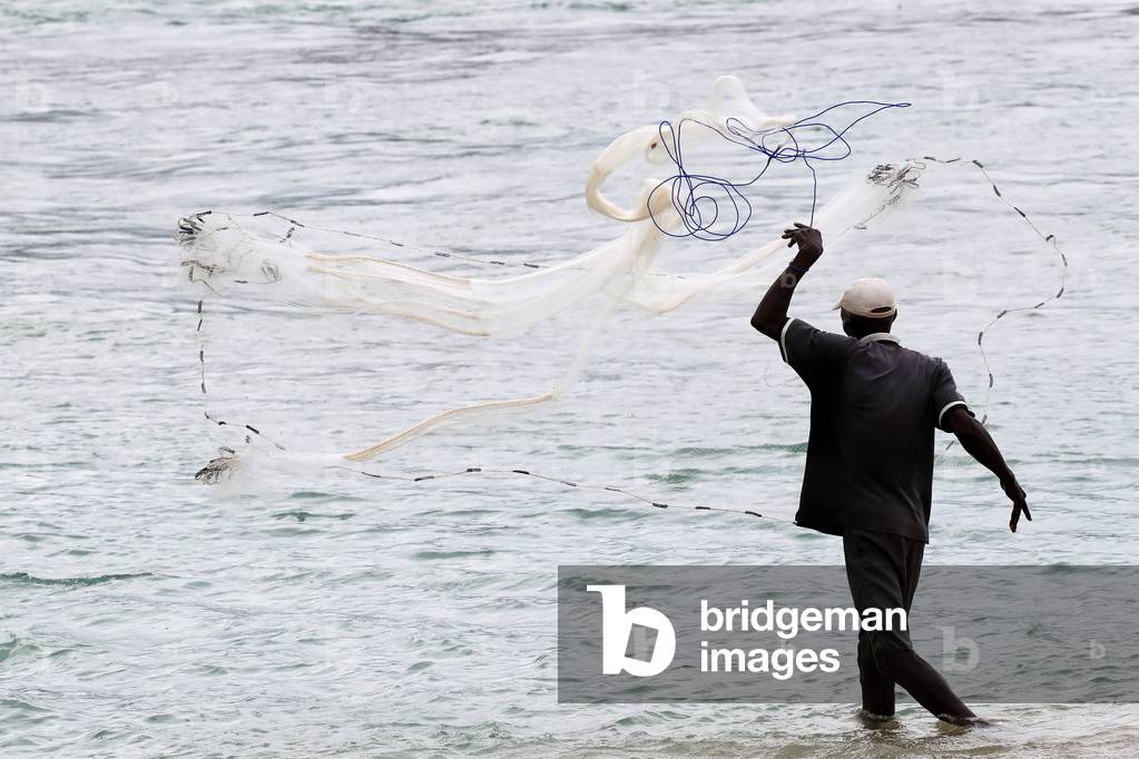 African fisherman throwing net into the sea in traditional way, Aneho, Togo, 2019 (photo)
