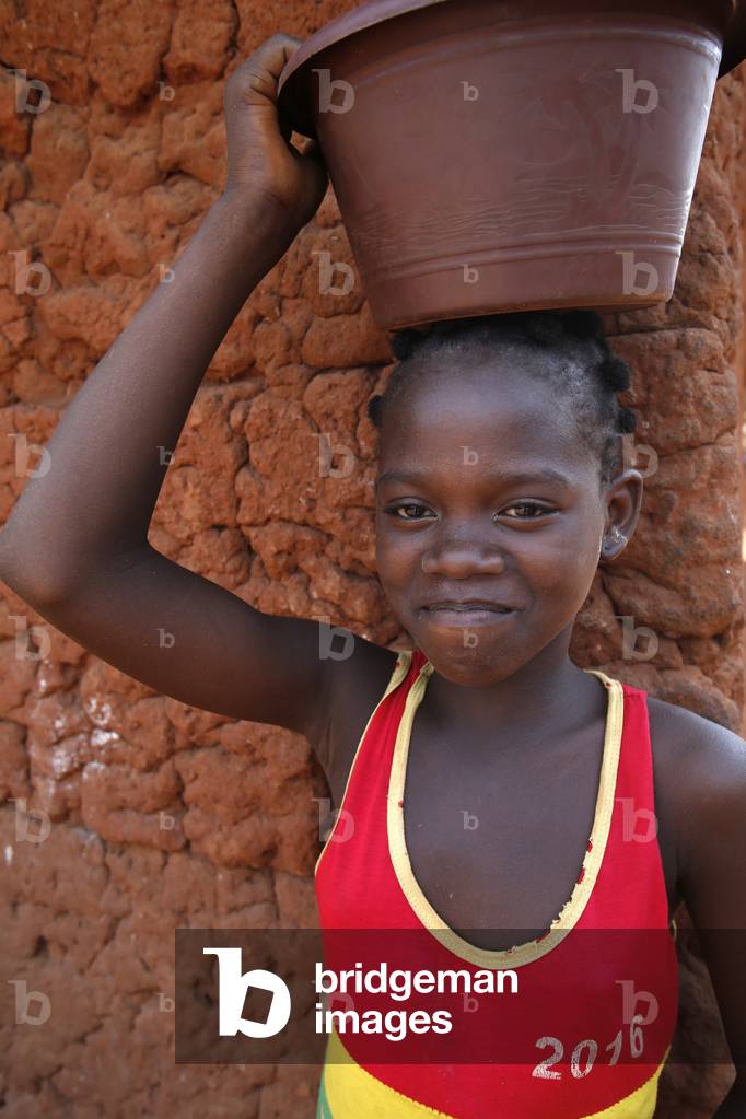 Girl carrying a bucket on her head in a Zou province village, Benin, Africa (photo)