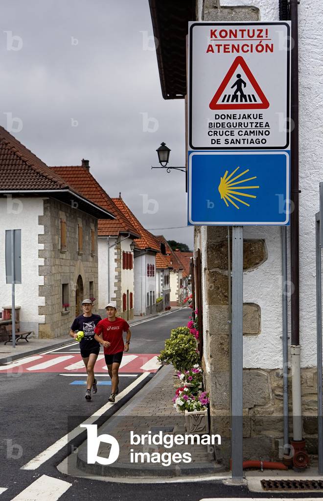 Bilingual sign on the way to Santiago de Compostela, two walkers