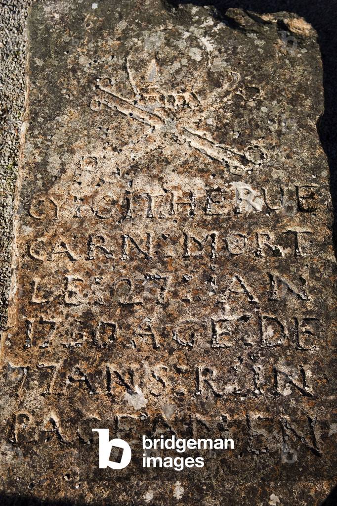 Old gravestone carved in French writing and a skull and crossbones.