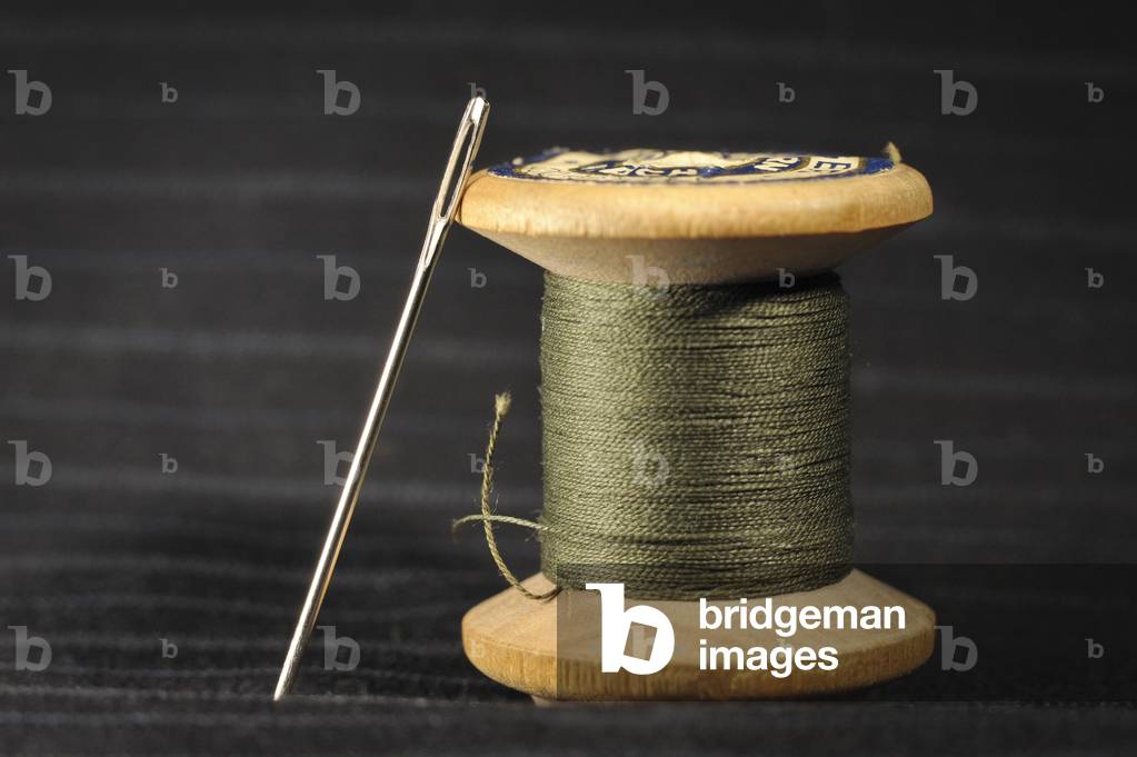 Wooden spool with green thread and darning needle, on black striped cotton (photo)