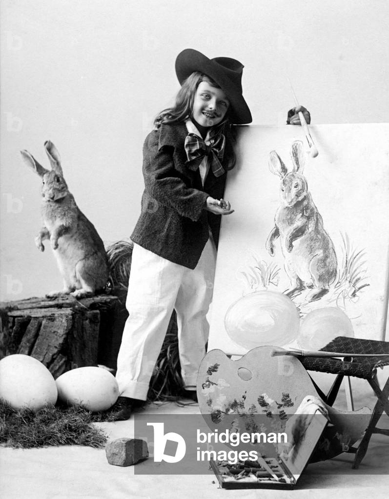 Easter party: young boy painting Easter rabbits with eggs on a canvas. Photography around 1915