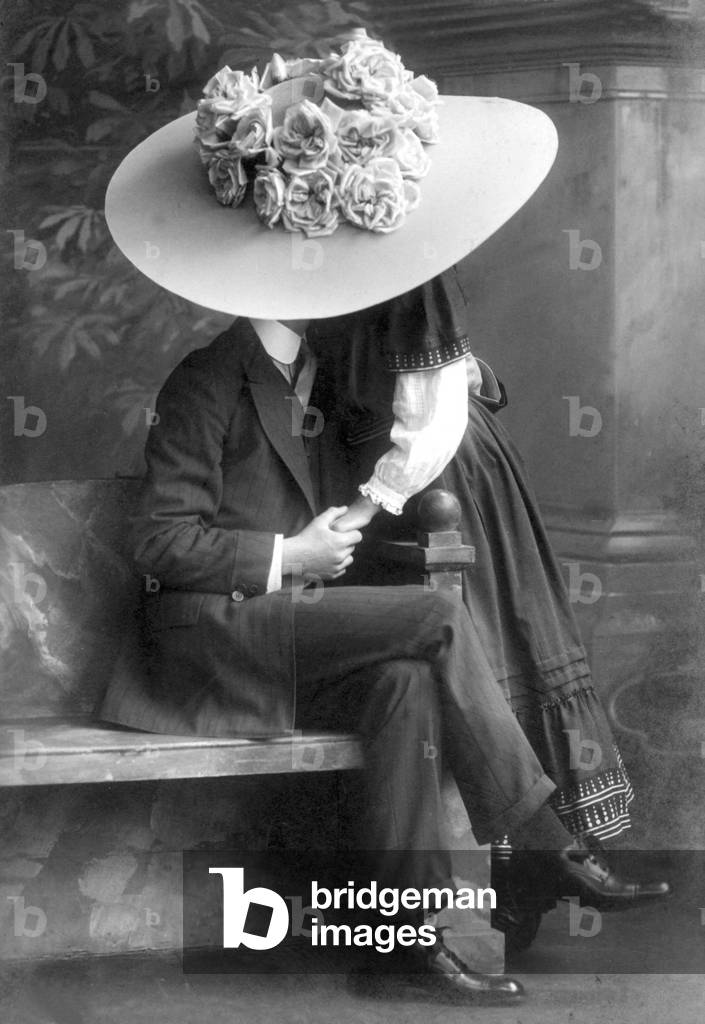 Young couple kissing under a huge hat.