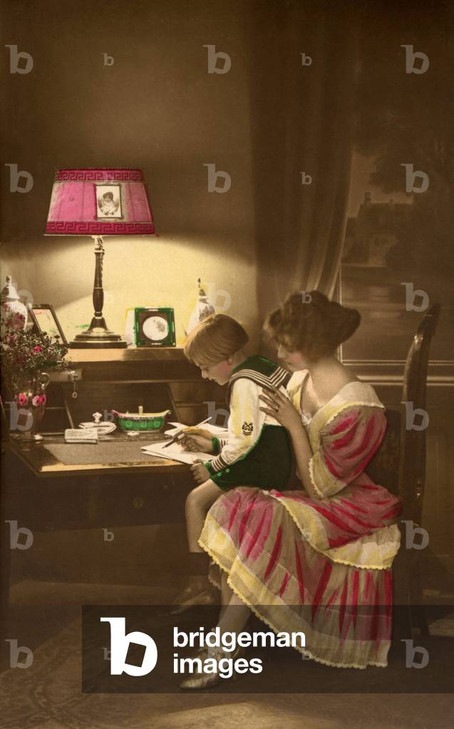 Mother and child on her knees in sailor's costume doing her homework. photograph around 1915.