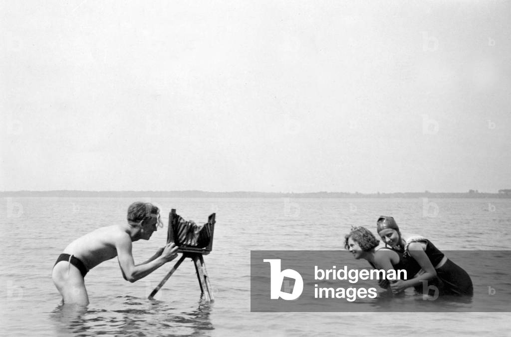 Photographer in the sea taking a photograph of two women having fun in the water in swimsuit. photograph around 1920