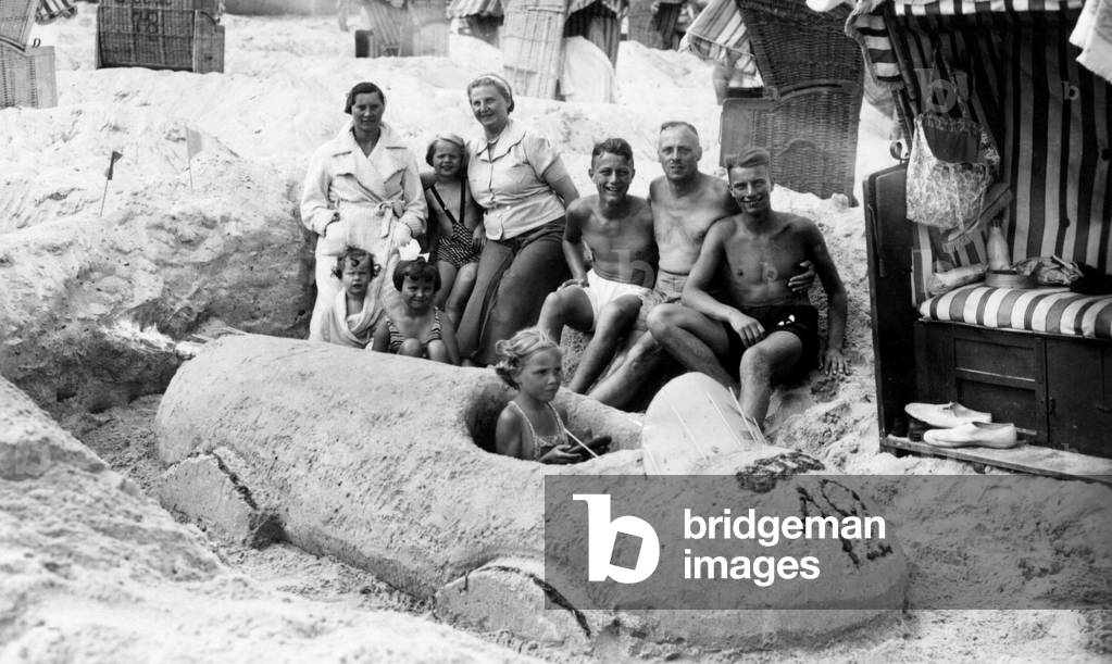 Family on the beach having built a car in the sand by the Baltic Sea. Photography around 1920