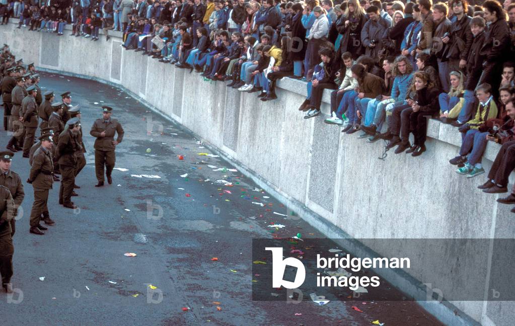 Berliners seated on wall facing GDR policemen near Brandenburg Gate on november 10, 1989 (photo)