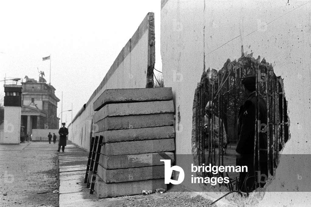 Holes in the wall at the level of the Brandenburg Gate watched by East German guards, December, 1989 (b/w photo)
