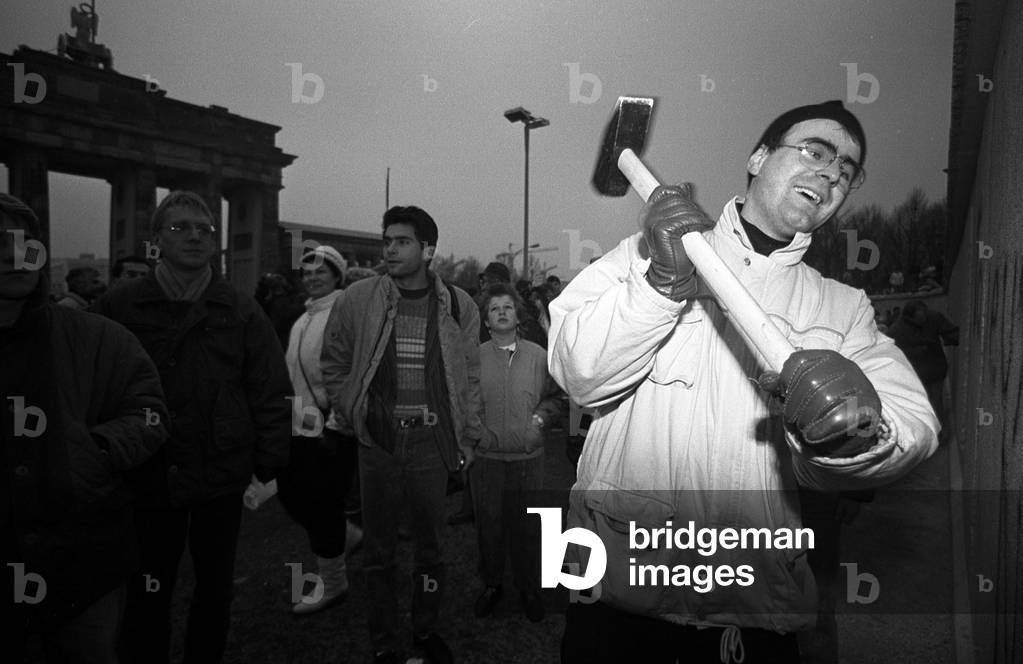 West Berliners passed through the no man's land area outside the Brandenburg Gate while a man attacks the wall with a hammer, 11 November, 1989 (b/w photo)