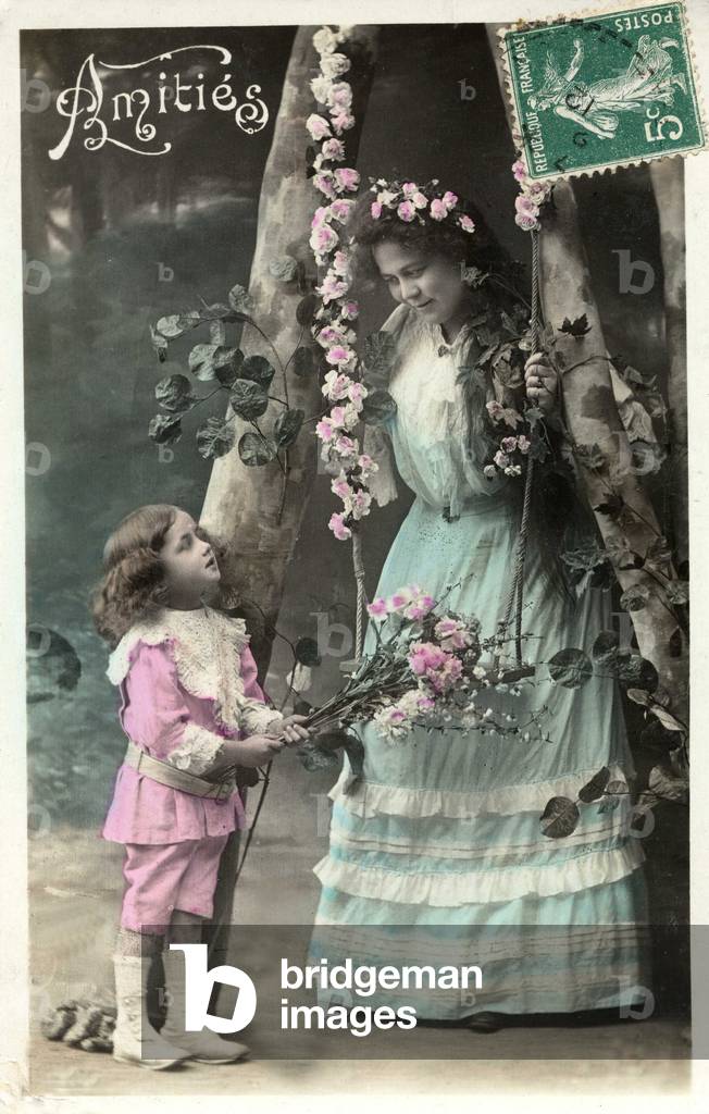 "Biglietto di auguri raffigurante una donna e un bambino vicino a un'altalena fiorita. Cartolina dell'inizio d