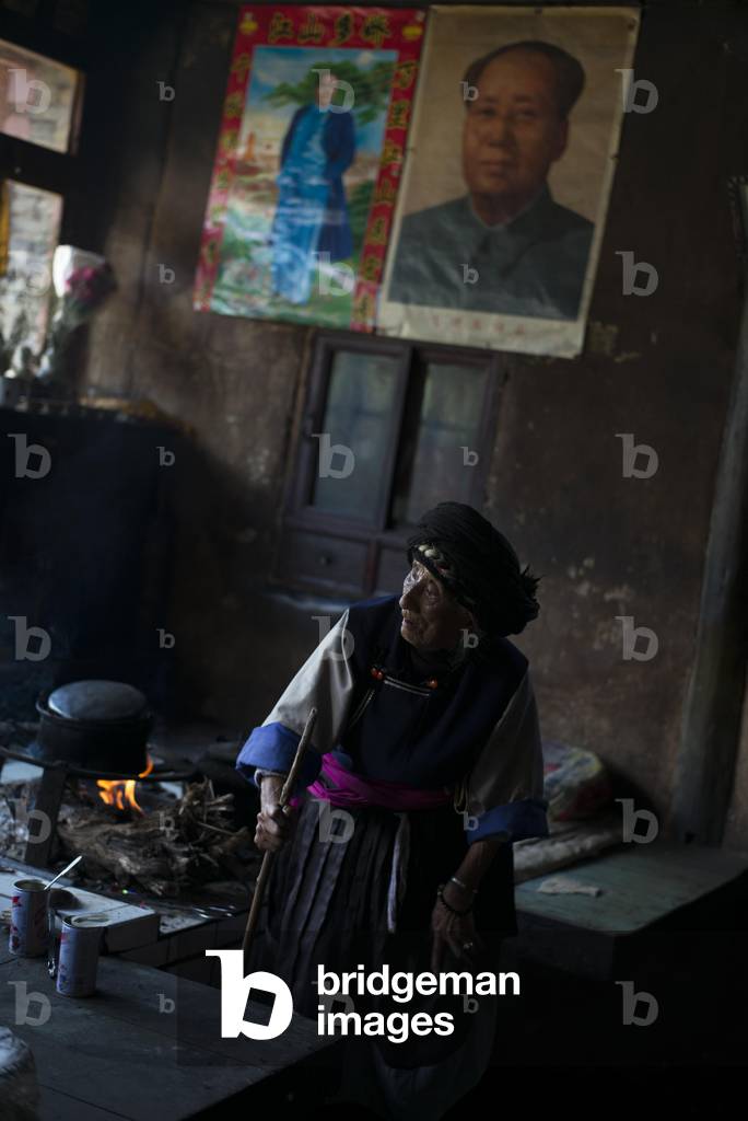 Old lady in Yunnan getting her food ready with Moa poster on wall, China (photo)