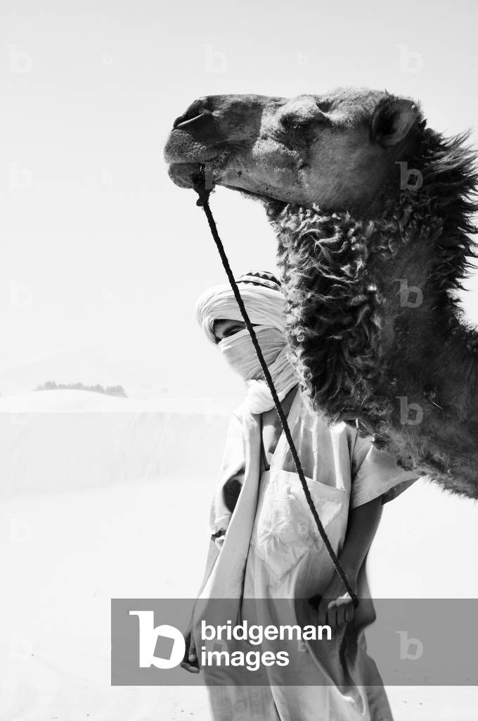 Portrait of young man with his camel in Erg Chebbi, Sahara desert, Morocco (b/w photo)