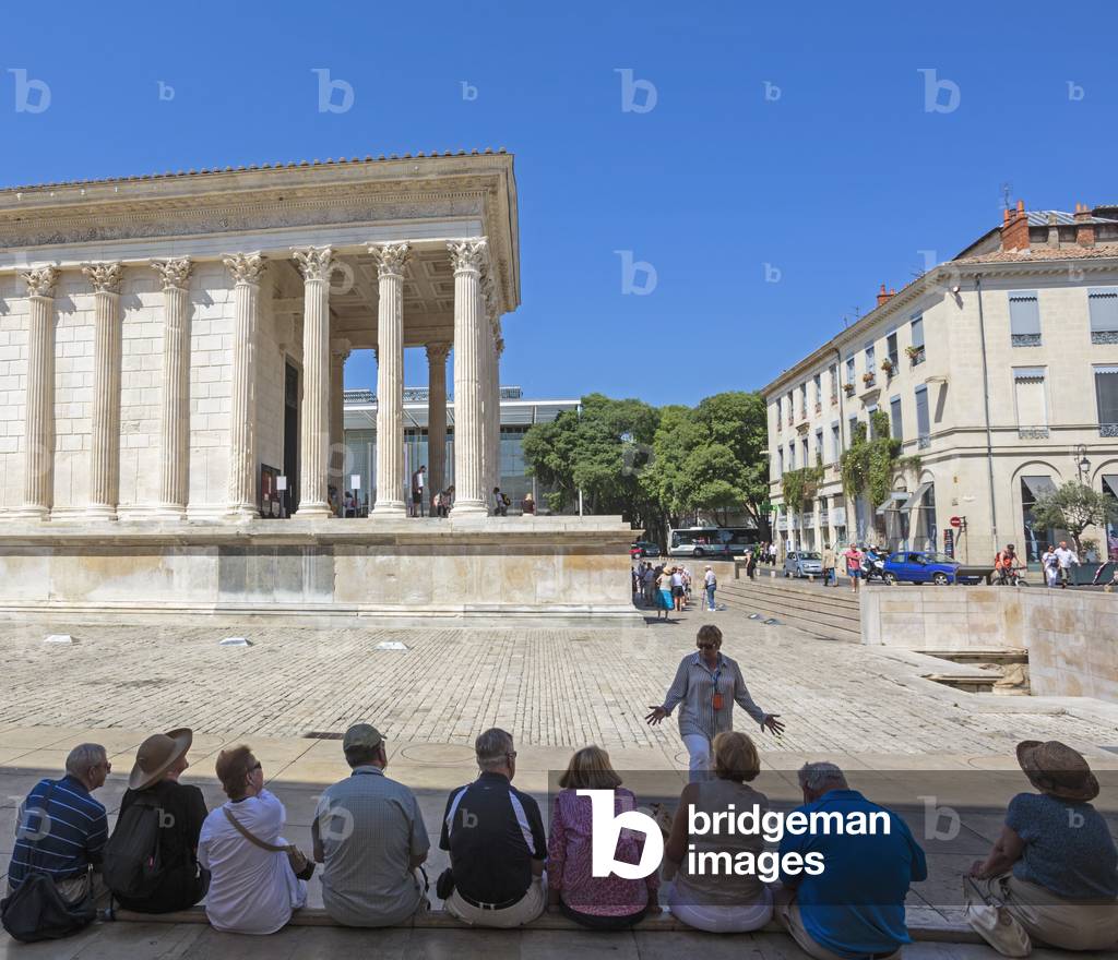 Nimes, Gard Department, Languedoc-Roussillon, France. A tour guide gives her group details of the first century BC Roman temple known as Maison Carree.