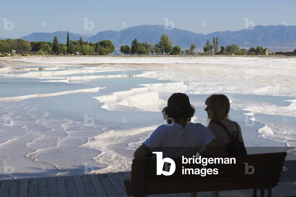Pamukkale, Denizli Province, Turkey.  A couple looking out over the white travertine limestone terraces and pools.  Pamukkale is known as the Cotton Castle.  It is a UNESCO World Heritage Site.