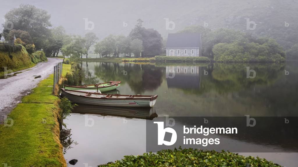 Gougane Barra, County Cork, Republic of Ireland.  Eire.  Looking across rowing boats moored at the lake shore with the Hermitage of St. Finbarr in the mist in the background. (photo)