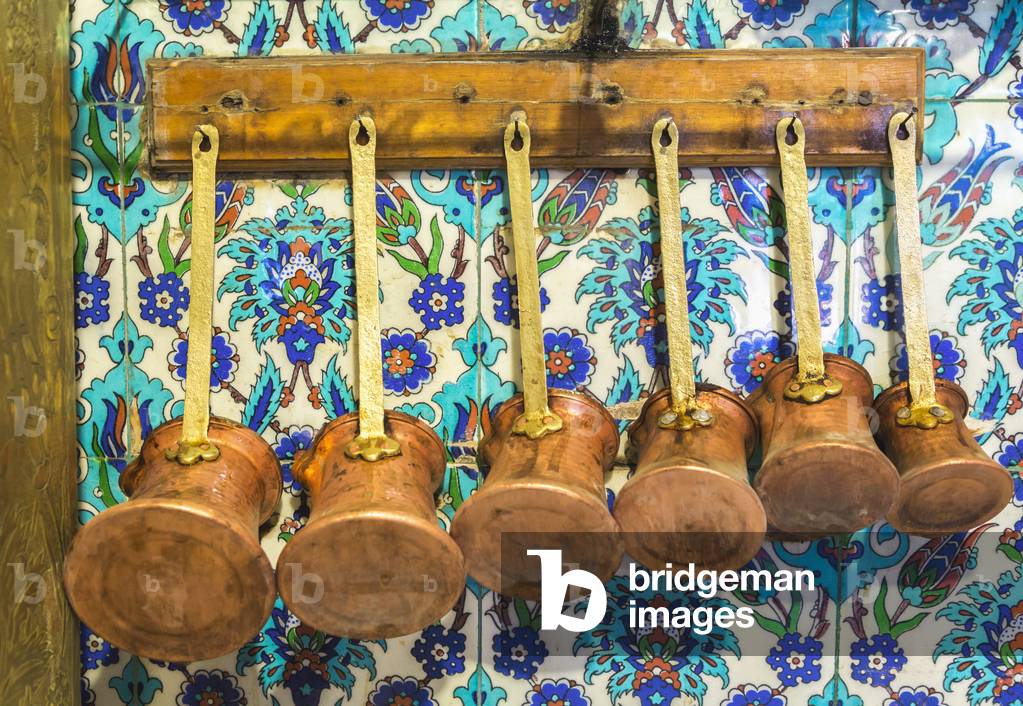 Istanbul, Turkey.  Various sized pots for preparing Turkish coffee hanging in a cafe kitchen.  Typical tiles on wall.