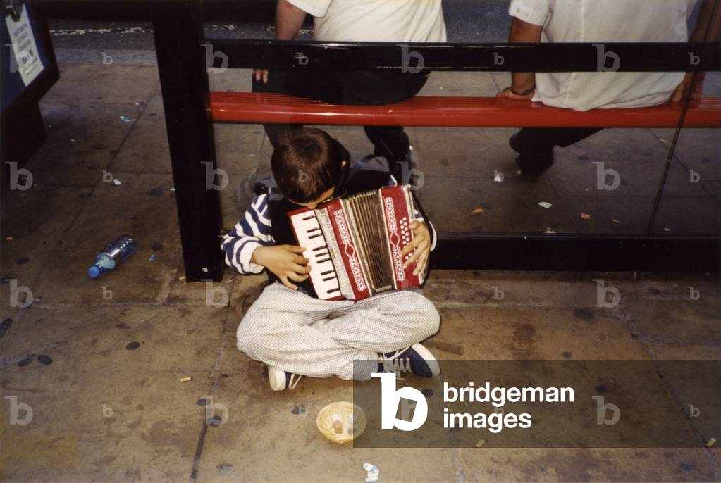 Small child playing accordion by bus-stop in London