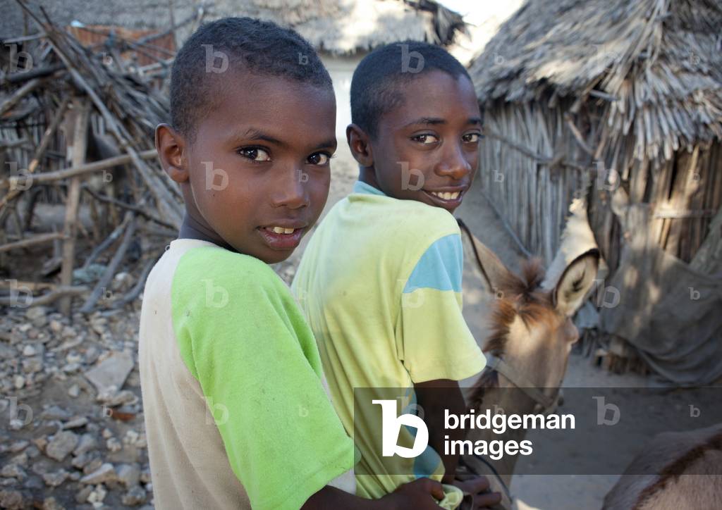 Two young boys riding one mule in the slums of lamu, Kenya, Africa (photo)