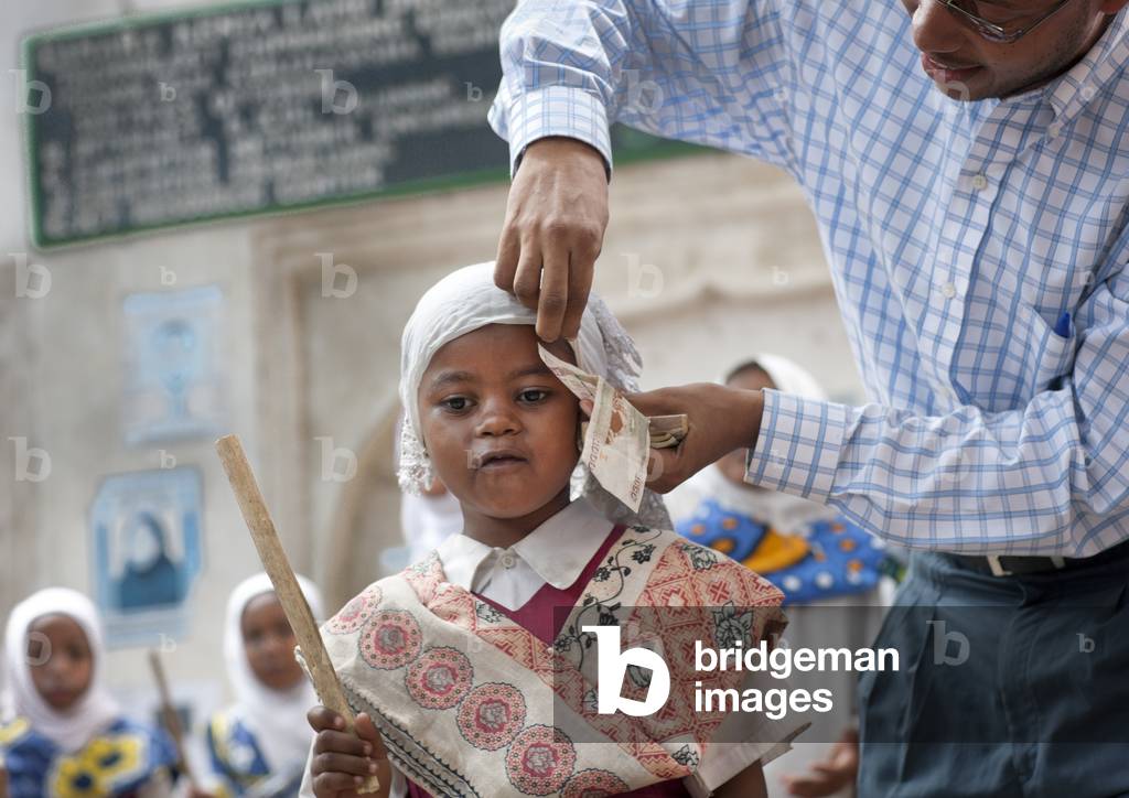 Man putting banknote under young girl's veil in traditional suit and holding a stick, Maulidi, Lamu, Kenya, Africa
 (photo)