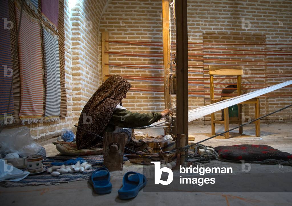 An old woman making a carpet in a caravanserai, Yazd Province, Meybod, Iran (photo)