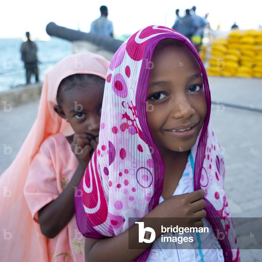 Two young girls with color veil passing by the dockside of lamu, Kenya, Africa (photo)