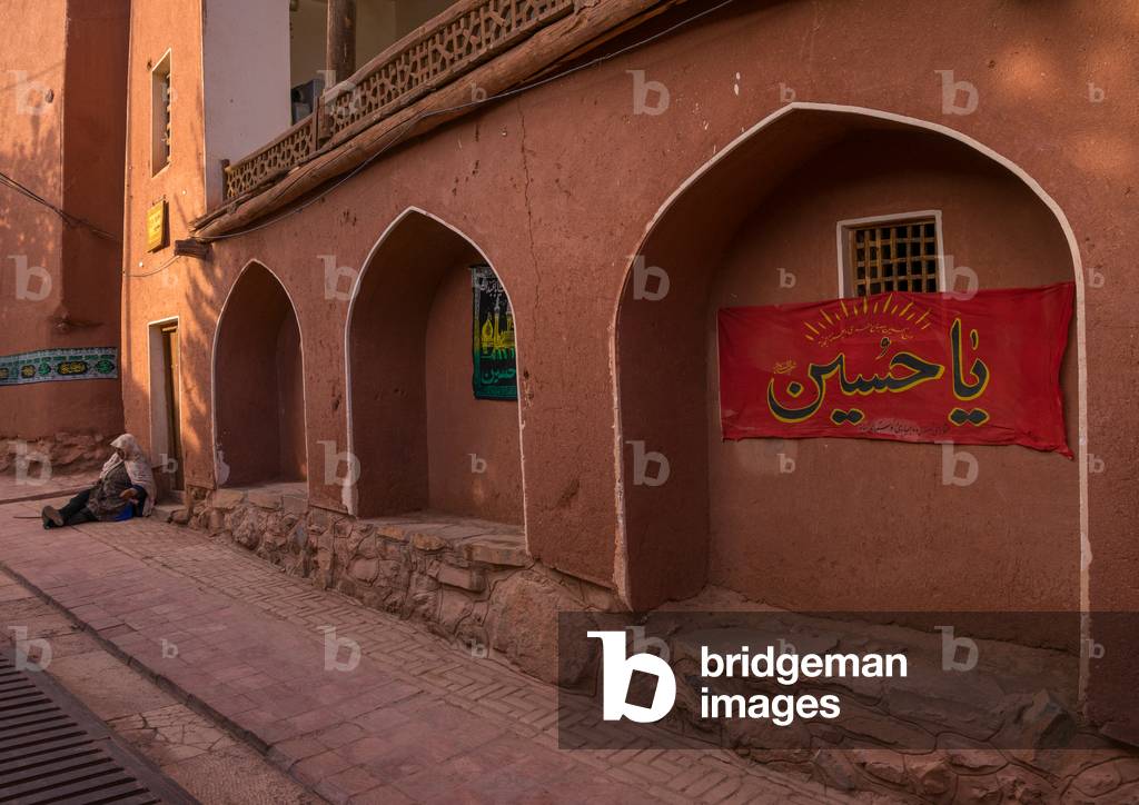 Woman Sitting in front of an Ancient Building with Ashura Decoration in Zoroastrian Village, Isfahan Province, Abyaneh, Iran (photo)