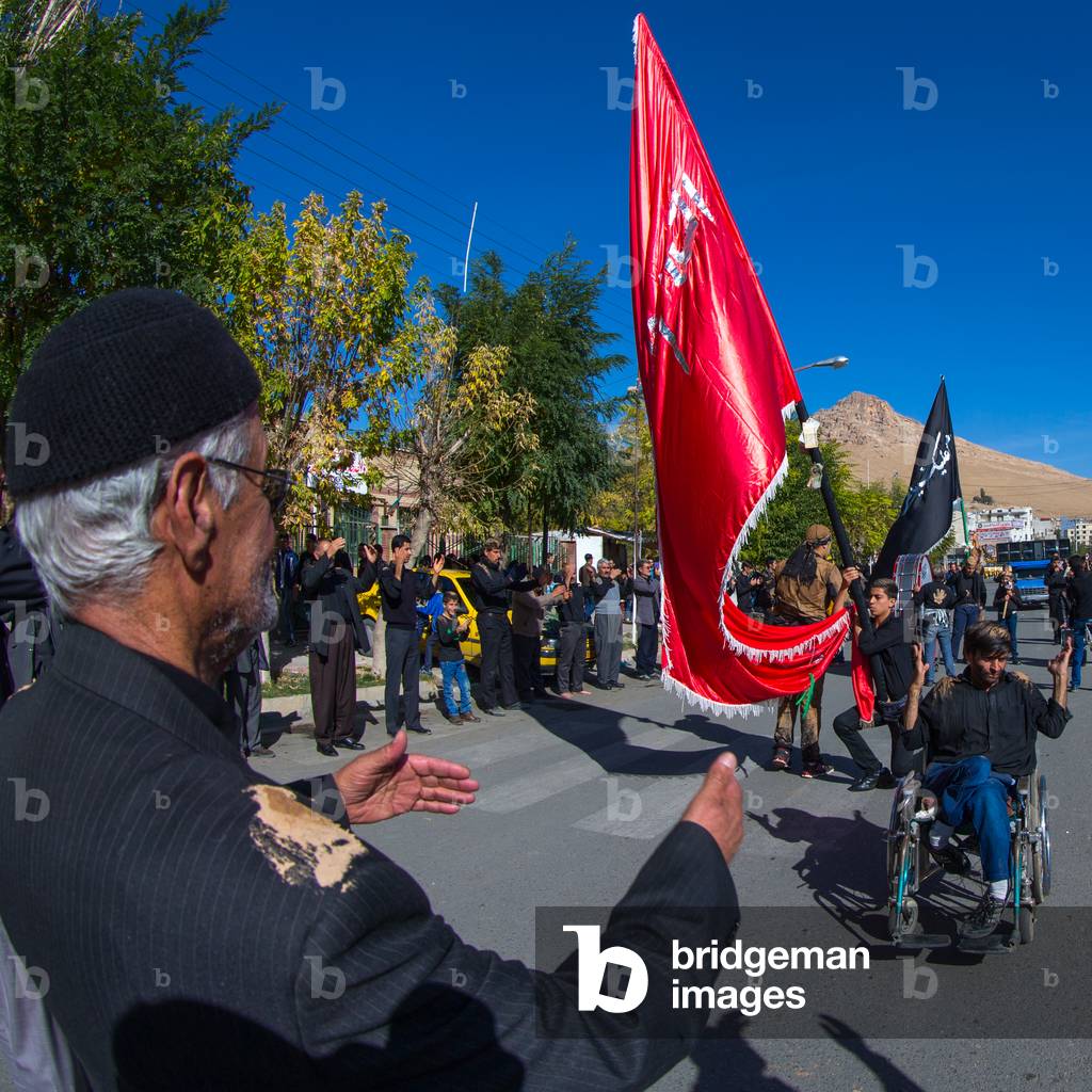 Man in Wheelchair in front of a Red Flag Celebrating Ashura, Kurdistan Province, Bijar, Iran (photo)