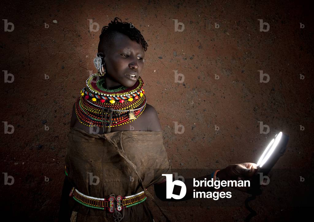 Turkana tribe woman with huge necklaces and earrings looking at a torch, Turkana lake, Loiyangalani, Kenya, Africa (photo)