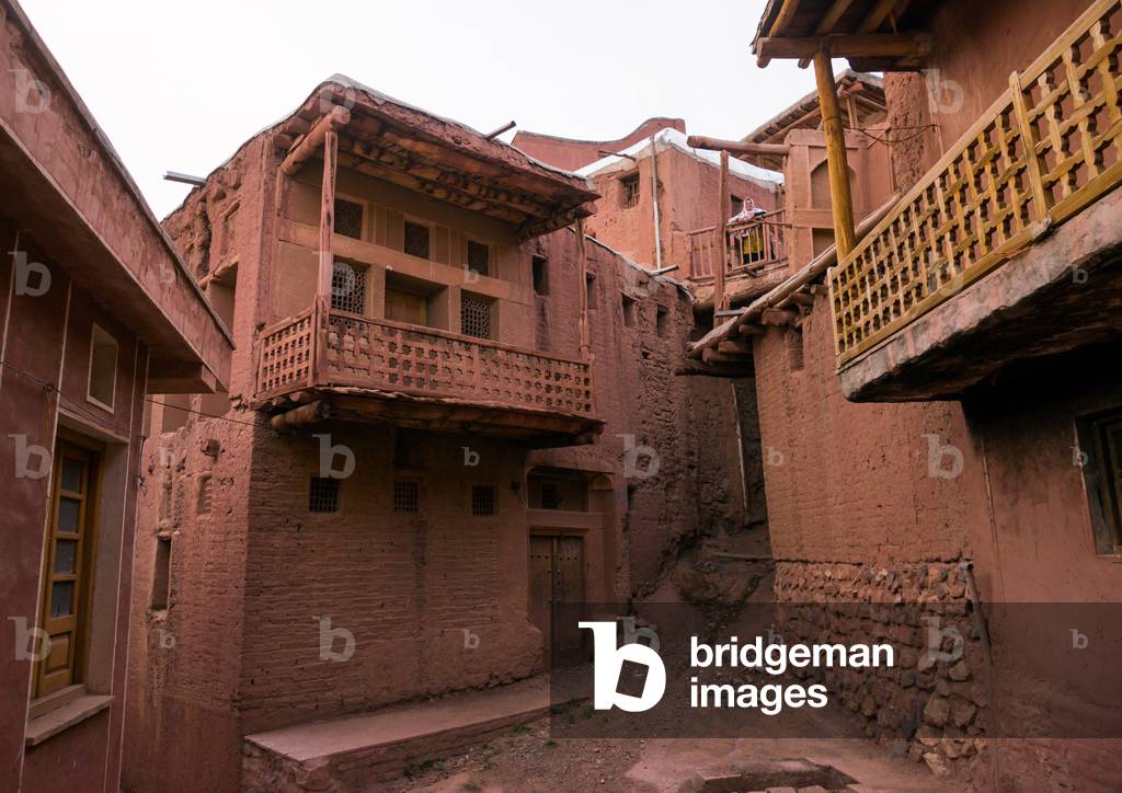 Iranian Woman Standing at the Balcony of an Ancient Building in Zoroastrian Village, Isfahan Province, Abyaneh, Iran (photo)