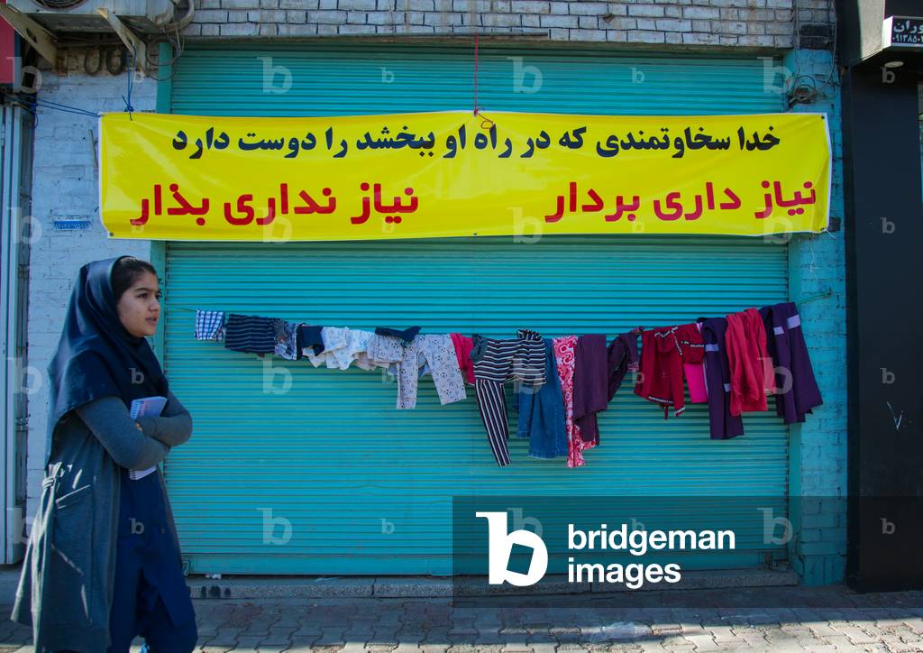 Woman Passing In Front Of A Wall Of Kindness Created To Give Clothes For Free To Poor People, Central County, Yazd, Iran, 2016 (photo)