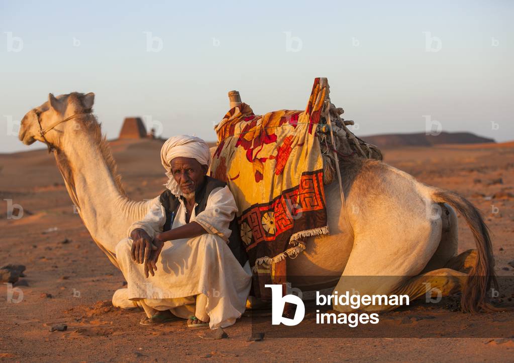 Man And His Camel in Front of The Pyramids And Tombs in Royal Cemetery, Meroe, Kush, Sudan (photo)