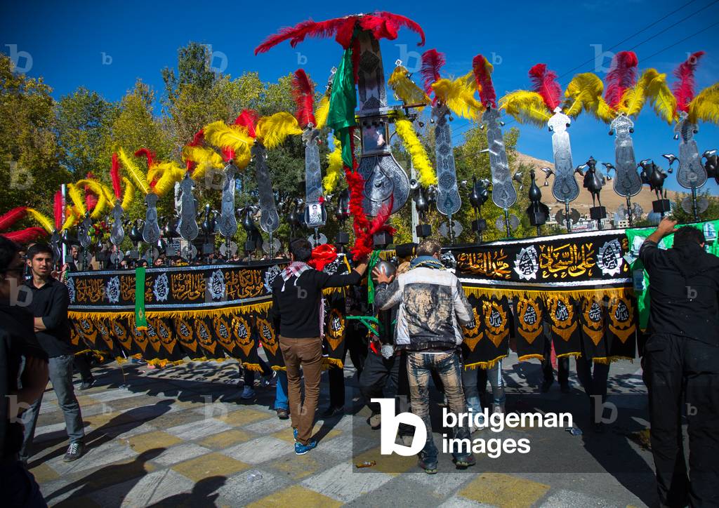 An Iranian Man carrying an Alam helped by Shiite Muslim Mourners, Isfahan Province, Kashan, Iran (photo)