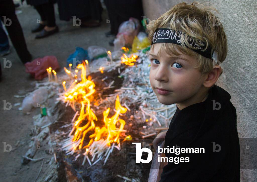 Iranian boy lights candles during Chehel Manbar ceremony on Tasua to commemorate the martyrdom anniversary of hussein, Lorestan Province, Khorramabad, Iran (photo)