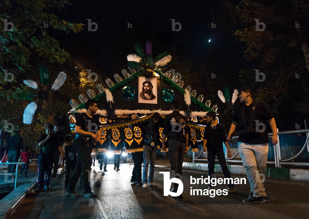 An Iranian man carrying an alam is helped by shiite muslim mourners to keep his balance during Muharram, Central County, Theran, Iran (photo)