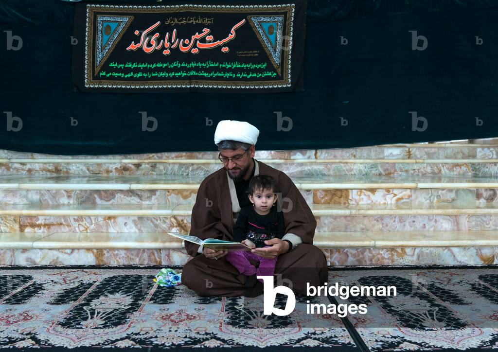 Mullah with his daughter in the Shrine of sultan Ali during Muharram, Kashan County, Mashhad-e Ardahal, Iran (photo)