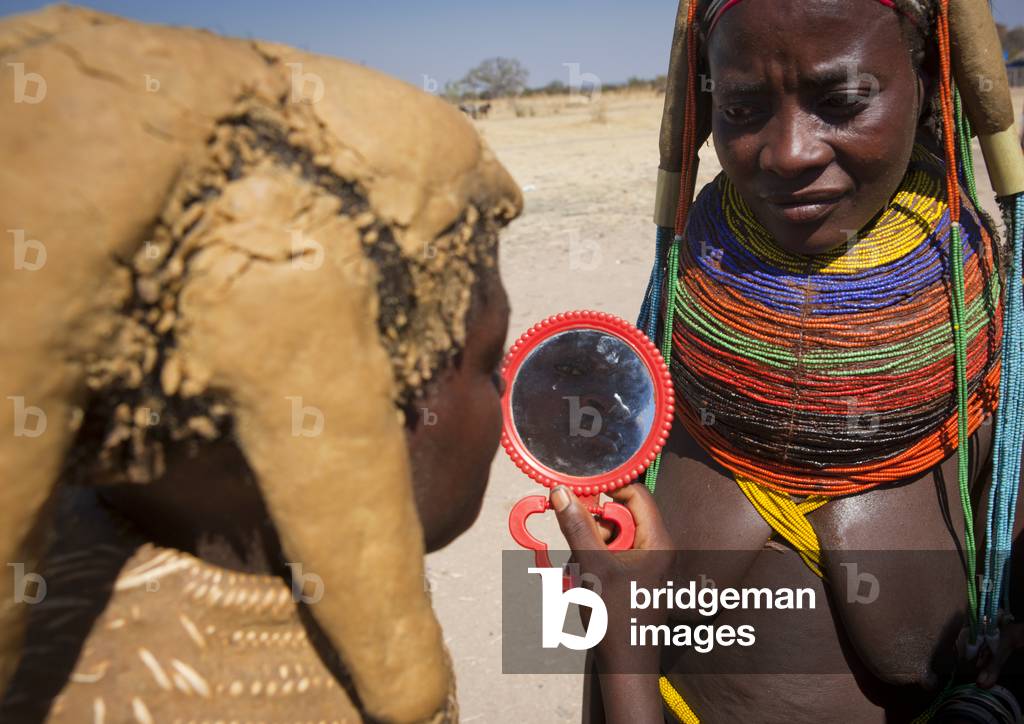 Mumuhuila Girl looking at Herself in a Hand Mirror, Hale Village, Angola, Africa (photo)
