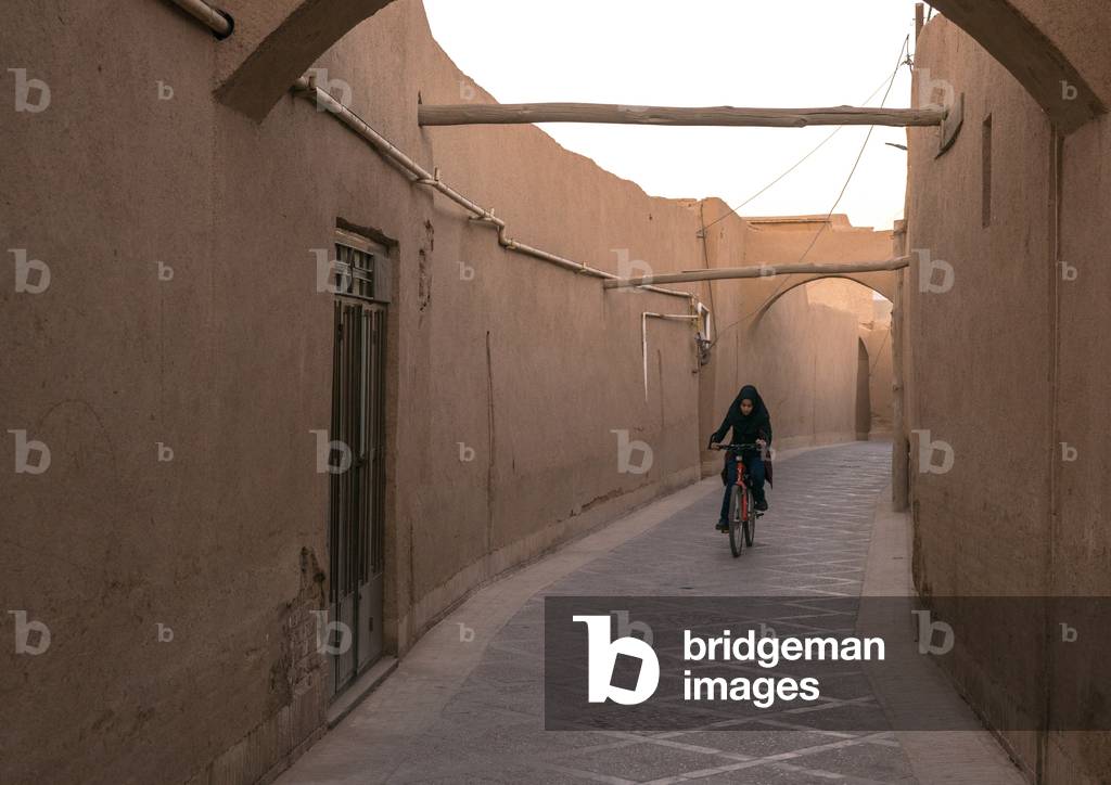 Girl Riding a Bicycle in a Narrow Street, Yazd Province, Yazd, Iran (photo)