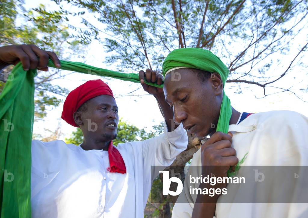 Red turbanned man putting white turban on another boy's head, Maulidi, Lamu, Kenya, Africa (photo)