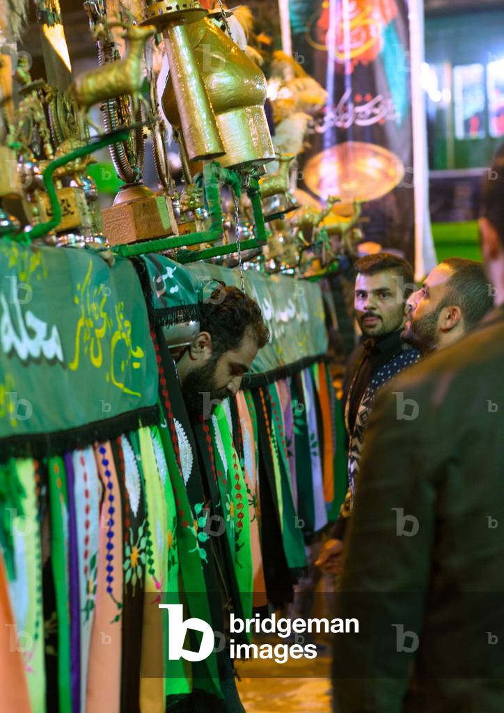 An Iranian Man carrying an Alam helped by Shiite Muslim Mourners, Golestan Province, Gorgan, Iran (photo)