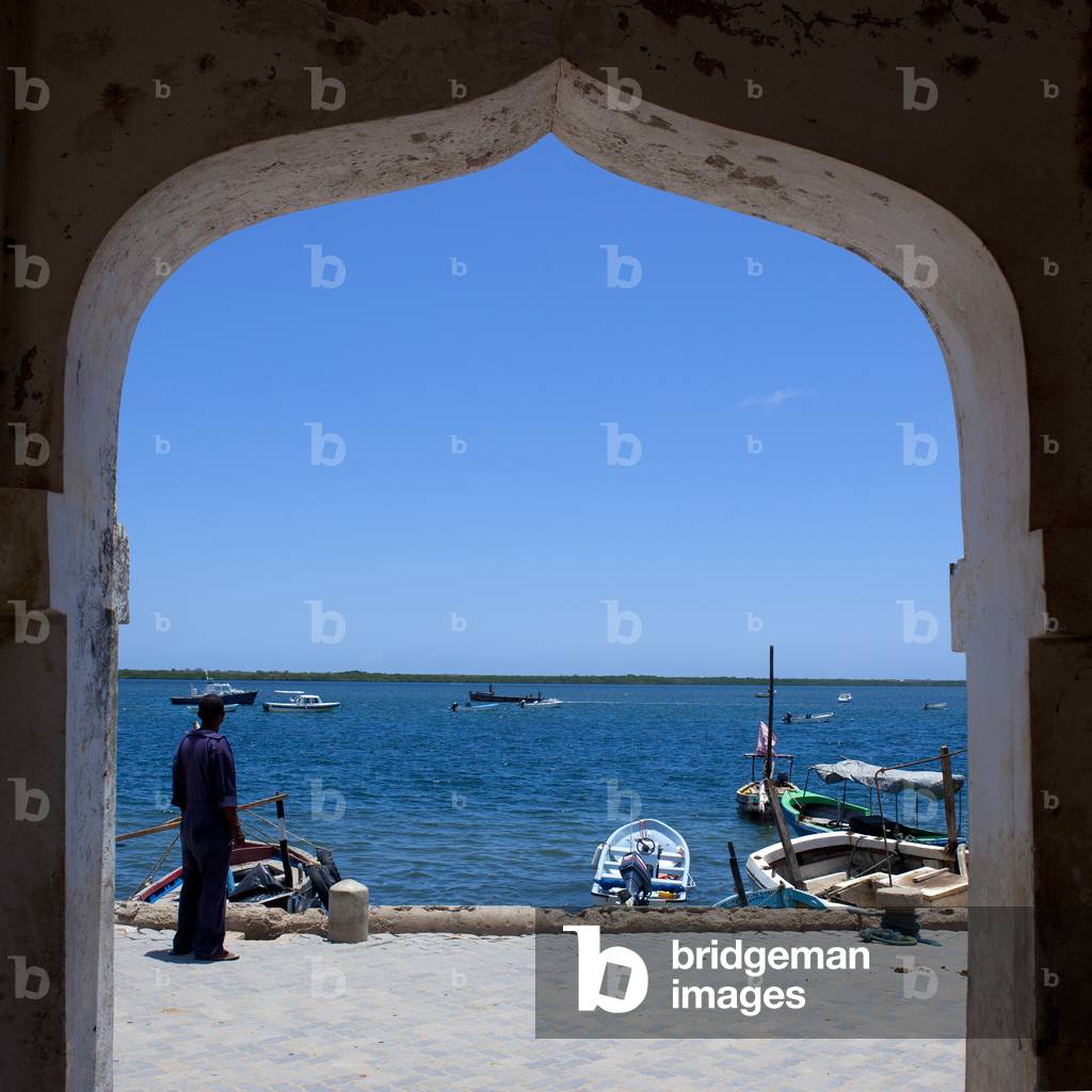 See view from arch doorway frame, One man standing on dockside, Lamu, Kenya, Africa (photo)