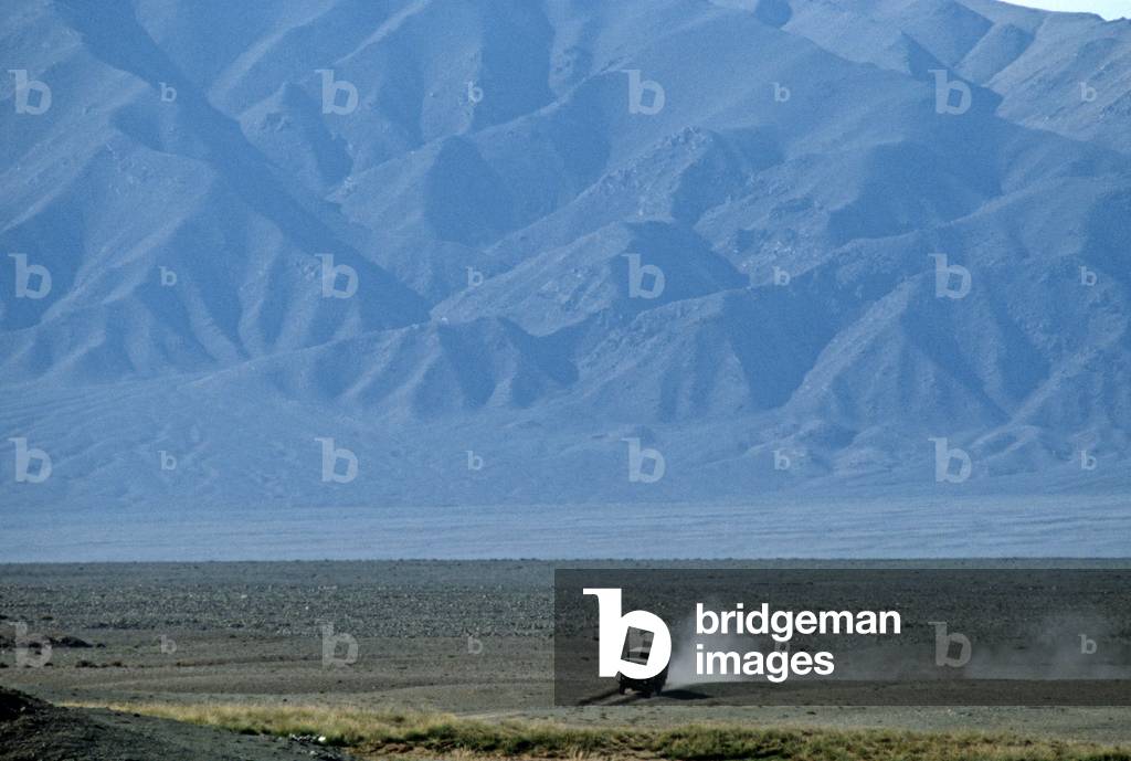 Truck driving through Gobi desert with Gobi-Altai Mountains in background, Mongolia, Asia