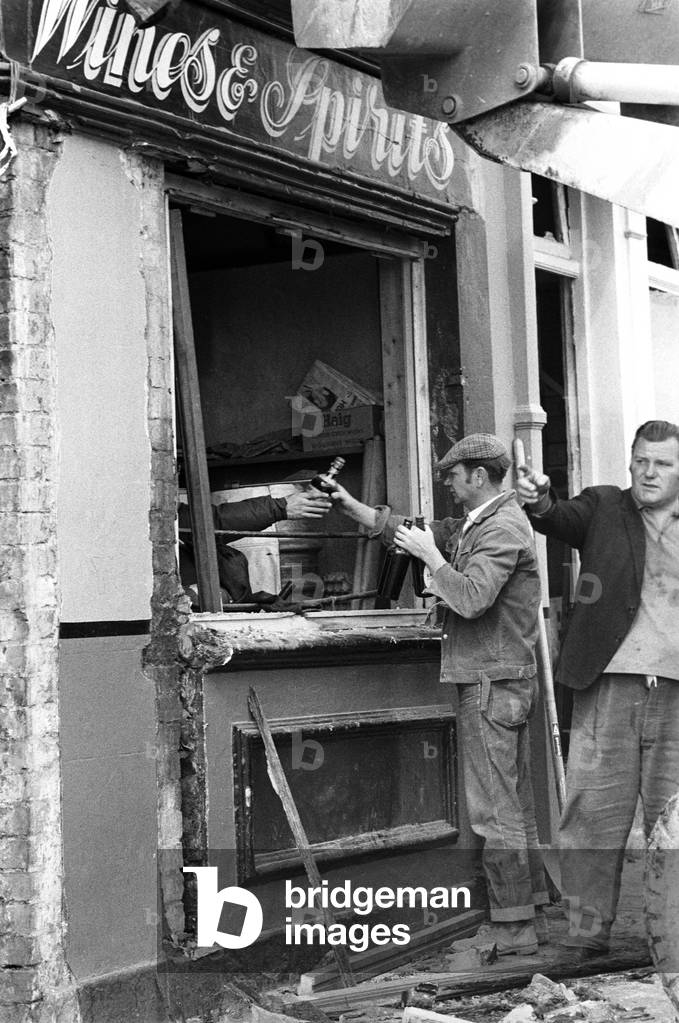 Collecting bottles from a Loyalist pub after an IRA bomb in Belfast, Northern Ireland,1974 (b/w photo)