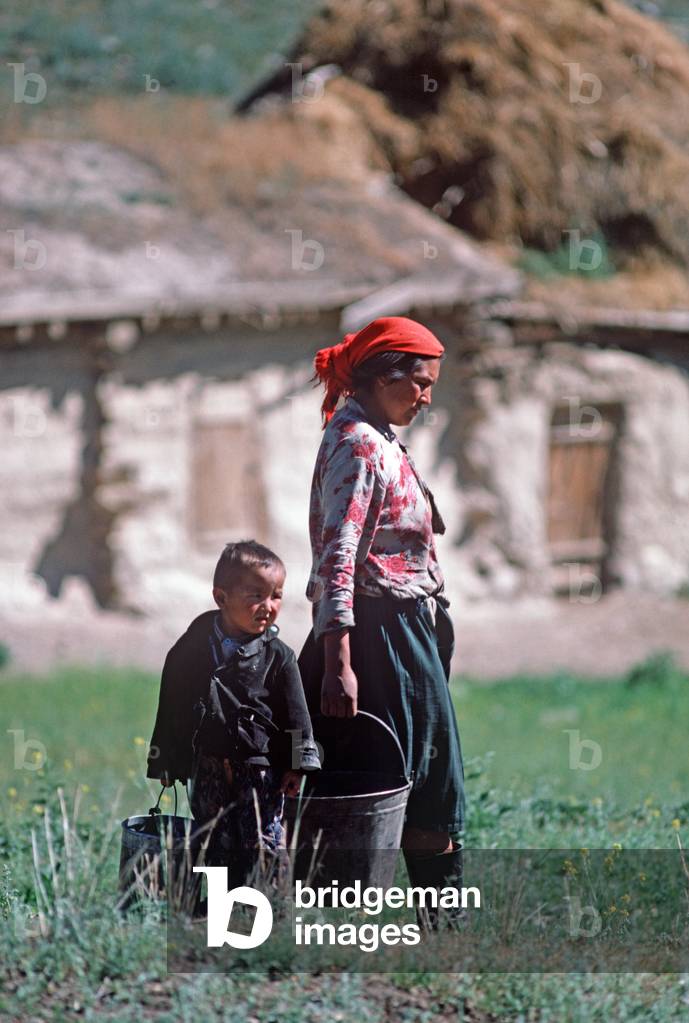 Kazakh mother and son carrying water buckets from farmhouse in hills North of Urumqi, Xinjiang Province, China (photo)