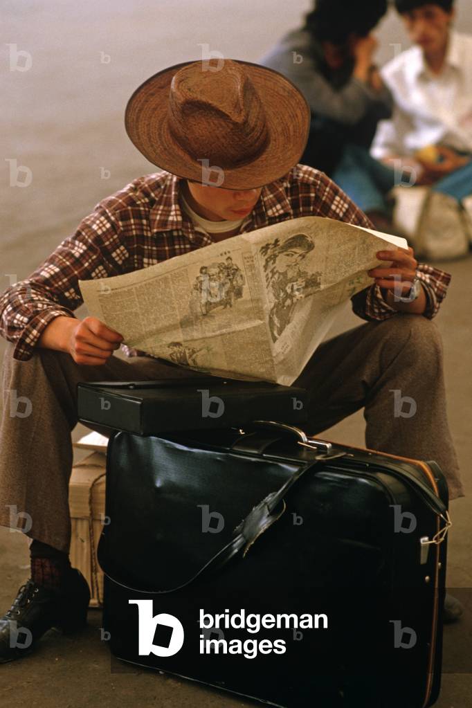Traveller reading newspaper outside Hangzhou Railway Station, Hangzhou, Zhejiang Province, China (photo)