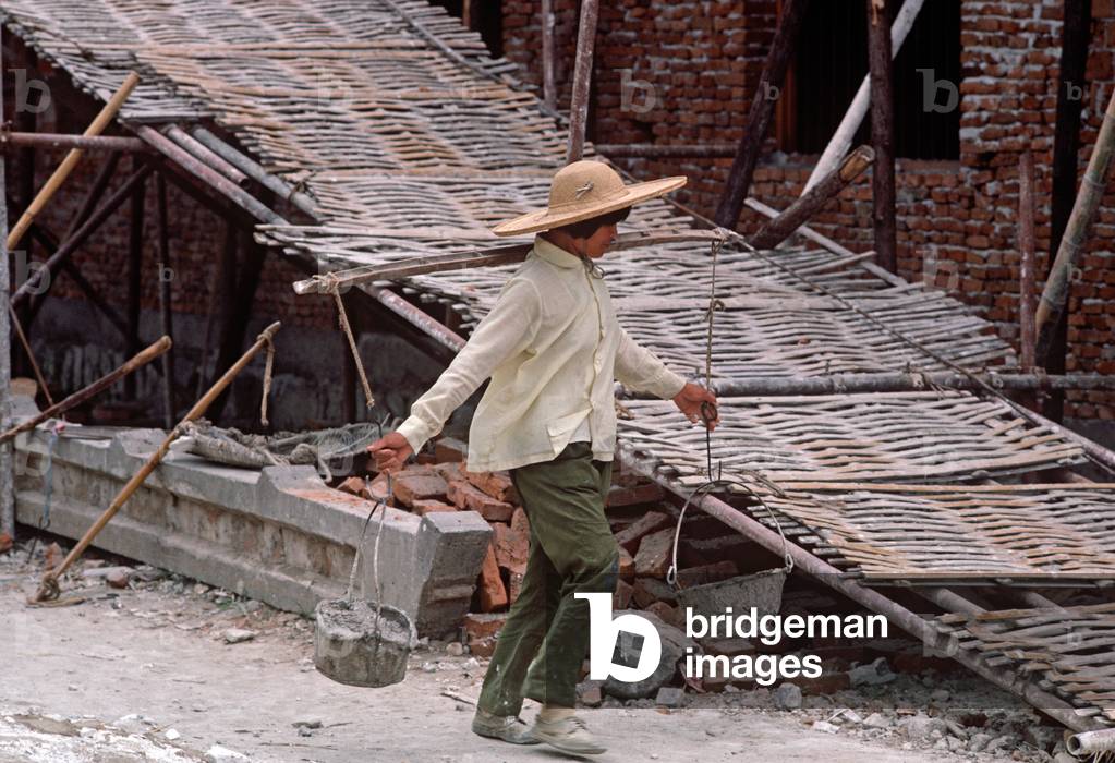 Chinese woman building labourer carrying cement onto building site, Shaoxing, China (photo)