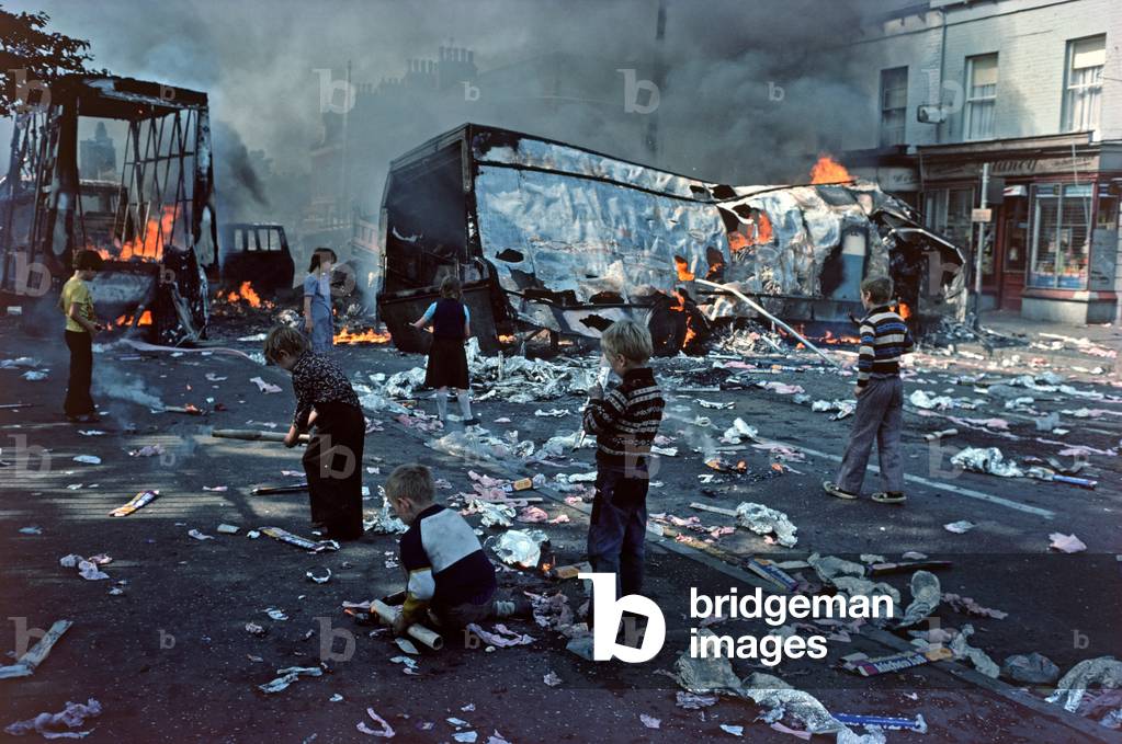 Children playing amongst debris from Hijacked Burning Vehicles after Riots in West Belfast during The Troubles, Northern Ireland, 1976 (photo)