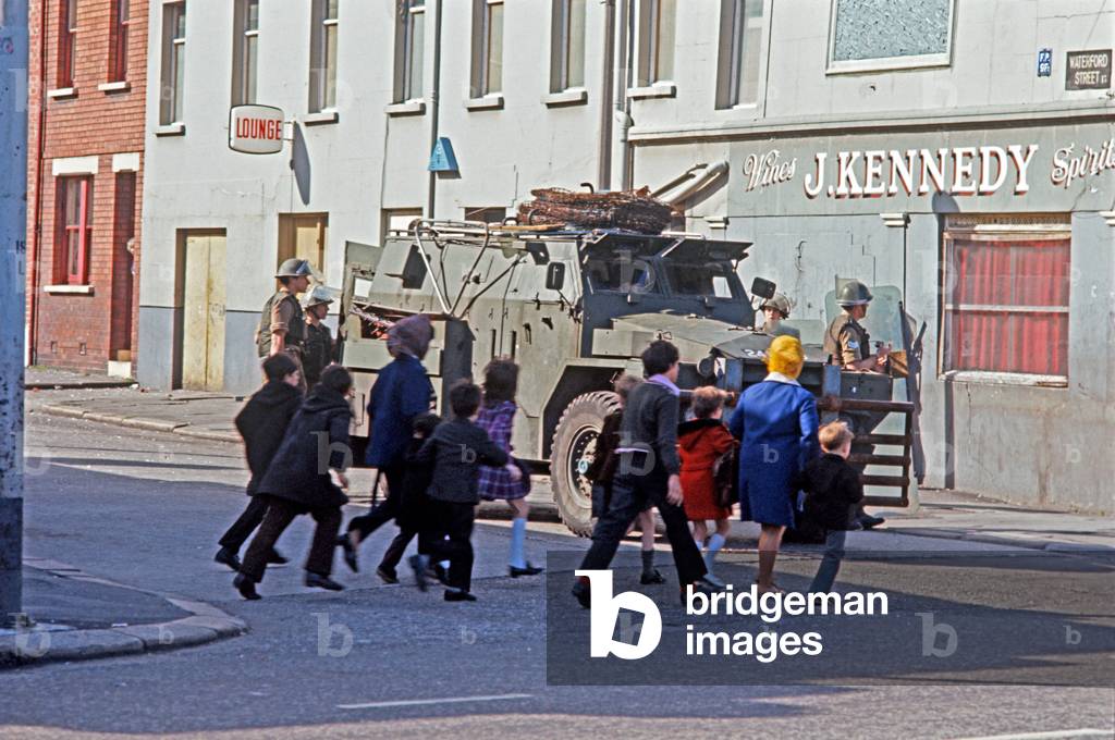 Families passing British Army Troops on streets of Belfast during The Troubles, Northern Ireland, 1972 (photo)