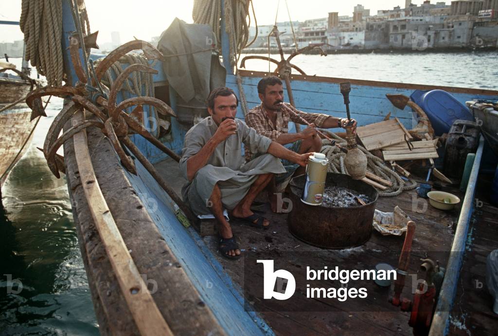 Sailors smoking water pipe on motorised Arab dhow, Dubai Creek, United Arab Emirates