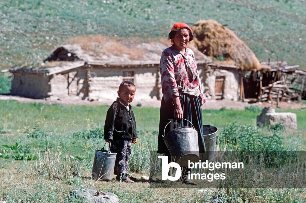 Kazakh mother and son carrying water buckets from farmhouse in hills North of Urumqi, Xinjiang Province, China (photo)